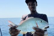 Angler holding a fresh catch of a red snapper against the ocean backdrop.