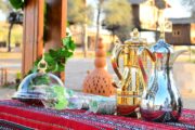 Two Arabic coffee pots displayed on a decorated table in an outdoor desert setting.