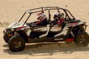 A group of riders in a Polaris dune buggy drifting through the desert, creating a sandstorm.