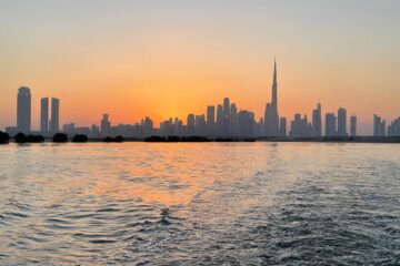 Dubai skyline at sunset with Burj Khalifa reflected over calm waters.