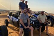 A group of friends posing with their Can-Am Maverick X3 dune buggy in the desert.