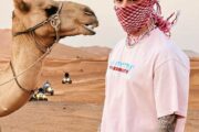 Tourist in traditional keffiyeh standing next to a camel in the desert