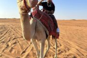 Tourist riding a camel in the desert with traditional attire