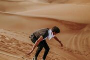 Man sandboarding down golden desert dunes