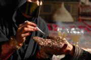 A woman meticulously applying intricate henna designs on another’s hand.