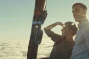 Romantic couple enjoying a sunrise hot air balloon ride above the clouds with a falcon.