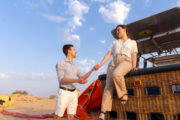 A couple standing near a hot air balloon, embracing while watching the flames ignite