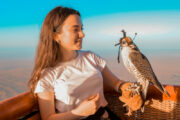 A young woman smiling while holding a falcon inside a hot air balloon.