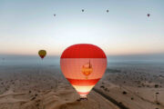 A fleet of hot air balloons soaring over the Dubai desert at sunrise.