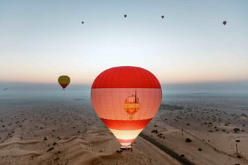 A fleet of hot air balloons soaring over the Dubai desert at sunrise.