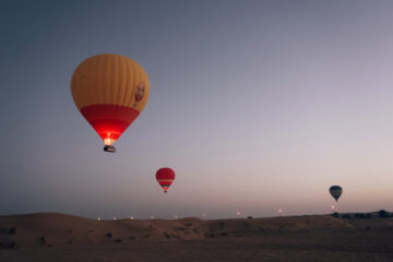 A hot air balloon floating above the desert landscape with green fields and roads.