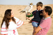 A smiling family holding a falcon in the middle of the desert.