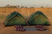 Two green dome tents placed side by side on desert sand.