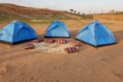 Three blue dome tents set up in the desert with floor cushions arranged in a circle.