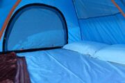 Interior view of a blue camping tent with bedding and pillows.