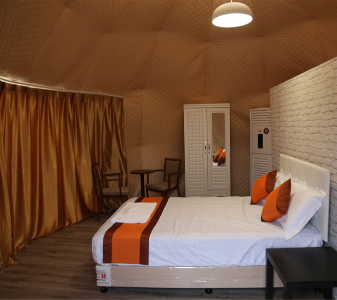 Interior tenda kubah premium yang nyaman dengan tempat tidur, lemari pakaian, dan area tempat duduk.