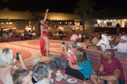 A belly dancer performing at a desert camp with guests watching.