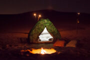 A cozy desert tent with a bonfire under the starry sky.