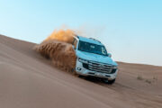 4x4 SUV kicking up sand while driving on desert dunes.