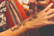 A close-up of an artist applying intricate henna designs on a woman's hand.