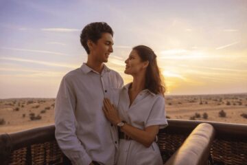 Romantic couple enjoying a sunrise hot air balloon ride above the clouds.