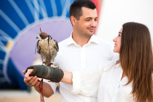 A couple enjoying a falconry experience in the Dubai desert, with a falcon perched on their hand.