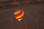 A colorful hot air balloon floating above the Dubai desert at sunrise.