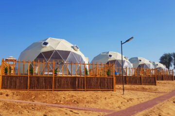 A row of large geodesic dome tents in a desert setting under a clear blue sky.