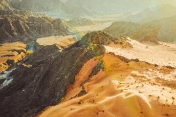 A striking aerial view of a desert mountain landscape with sunlit dunes.