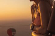 A couple enjoys a sunrise hot air balloon ride above the clouds.