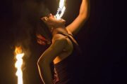 A fire performer dramatically consuming a flame in a nighttime show.