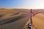 A woman standing on a sand board in a sunlit desert, poised for her next descent.