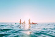 A group of four people on stand-up paddleboards silhouetted by the sun on a calm sea.