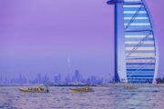 Two yellow tour boats gliding near the Burj Al Arab against a purple-hued sky.