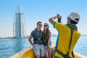 A couple posing for a photo on a yellow tour boat with the Burj Al Arab in the background.