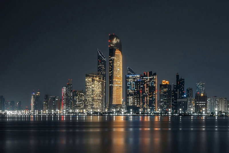 Abu Dhabi skyline illuminated at night, reflecting on the waterfront.