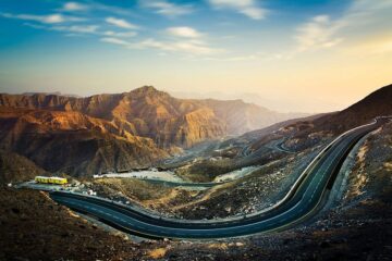 A bright mountain road lined by towering stone cliffs in Ras Al Khaimah.