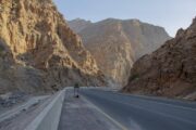 A paved mountain road winding between tall, rugged cliffs under clear daylight.