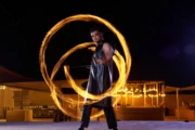 Male fire dancer twirling flaming rods in arcs around him.