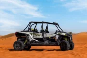 A Polaris RZR XP 1000 four-seater parked on the desert sand with a clear sky.