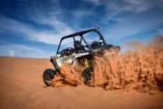 A Polaris RZR XP off-road buggy drifting across a steep dune, spraying sand.