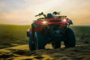 A red quad bike parked at dusk, headlights illuminated in the desert.