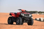 A red quad bike set against the sandy backdrop of a desert camp.