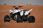 A white quad bike parked on red desert sands under a bright blue sky.