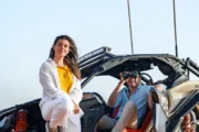 A man and woman standing beside a Can-Am buggy in the desert, one looking through binoculars.