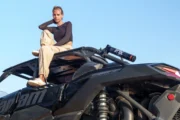 Woman perched on a Can-Am buggy, posing confidently in the desert.