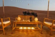 A cozy wooden seating arrangement set up in the desert with a dune buggy in the background.