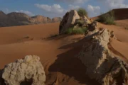 A small herd of camels grazing against a rocky desert backdrop under a clear blue sky.