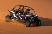 A four-seater dune buggy speeding across a vast, orange sand dune.