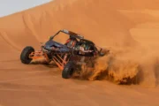 A dune buggy kicking up sand as it drifts along a steep desert slope